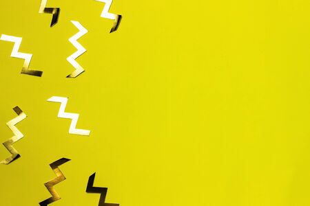 Gold zig zag shaped confetti on yellow background. Festive backdrop or banner. Top view, flat lay, copy space.の写真素材