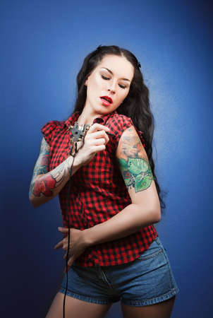 Photo of beautiful girl with tattoos and tattoo machine tattoing herselfの写真素材