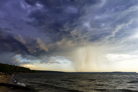 A terrible blue cloud with a heavy rainfall over the sea. Storm is coming to the beach.