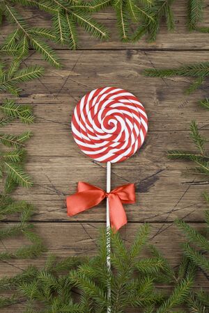 Christmas background. red lollipop with bow and tree branches on brown wood background. Close up. Copy space. new year card, flat lay, top viewの写真素材