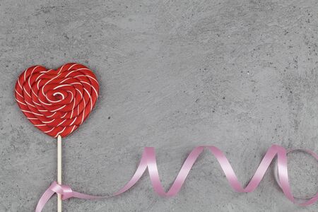 red heart as lollipop candy on gray background with ribbon. Valentines day minimalist background. love symbol, space for text concept. graphic design element for greeting cards, banners, saleの写真素材