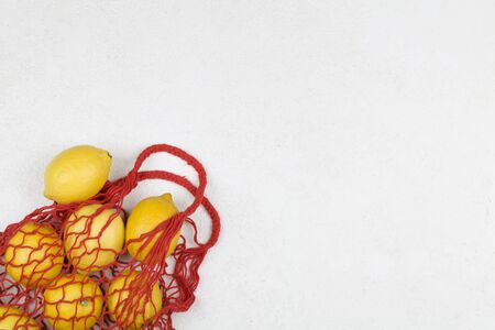 Red mesh shopping bag with yellow lemons on white background. Top view, flat lay, copy space. Zero waste, eco friendly concept.の写真素材
