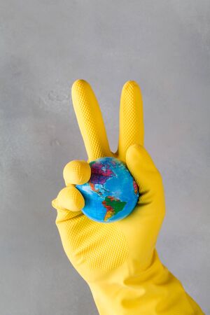 Human hand in yellow glove holds earth on blue background. Save planet from corona virus. reduce risk of infection and spreading the virus. victory concept over corona virus