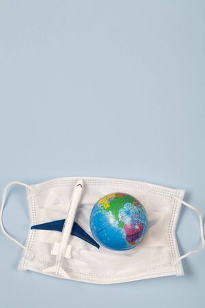 earth and toy airplane lying in medical mask on blue background. reduce risk of infection and spreading the virus. Concept of flight ban due to coronavirus pandemic. top view flat lay copy spaceの写真素材