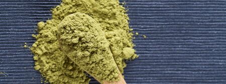 matcha green tea powder in wood spoon on blue background. top view copy space healthy food concept
