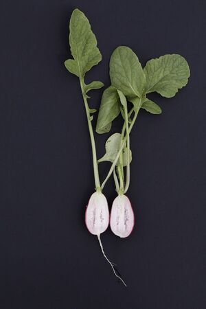 half cut radish with green leaves on black background. top view