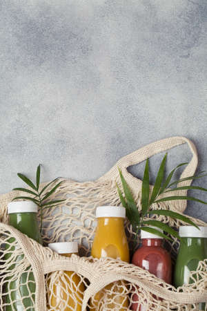 yellow green and crimson smoothie in mesh bag on blue background, served in bottle with palm leaf. healthy food concept. copy spaceの写真素材