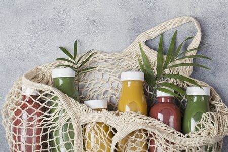 yellow green and crimson smoothie in mesh bag on blue background, served in bottle with palm leaf. healthy food concept.の写真素材