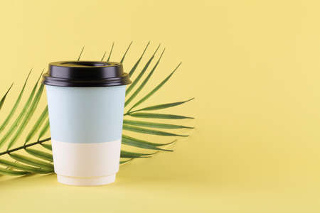 take away paper cup for coffee or tea on yellow background with green palm branch. copy space. minimal coffee concept.の写真素材