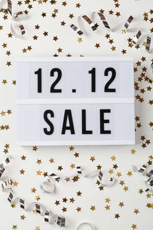 12.12 sale text on white lightbox, holiday ribbon and small stars on white