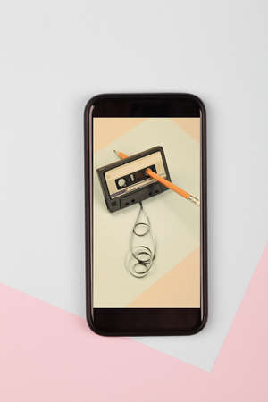 photo audio cassette with tangled tape on blue background with pencil on new mobile phone, minimalistic composition. retro and modern conceptの写真素材