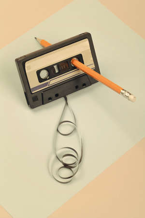 audio cassette with tangled tape on blue and beige background with yellow pencil, minimalistic composition. retro conceptの写真素材