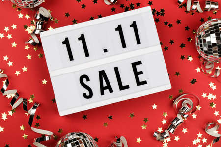 11.11 sale text on white lightbox, holiday ribbon, small stars and disco balls on red background. Online shopping, singles day sale concept. Top view copy spaceの写真素材