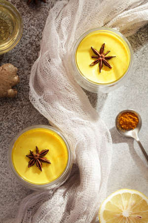 Turmeric, golden milk with lemon, spoon with turmeric powder, honey and textile on gray background....