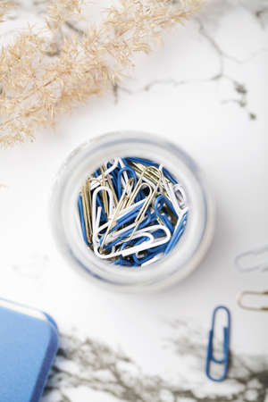 paper clips in glass jar with pampas grass and notepad on white background. working space. office...
