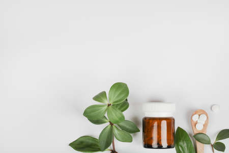 Herbal pills in glass bottle, wooden spoon and green plant leaves on white background. alternative medicine and healthy lifestyle concept. copy spaceの写真素材