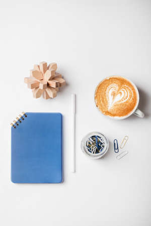 office desk workspace with notebook, pen, coffee, puzzle and paper clips in glass jar. Flat lay, top...