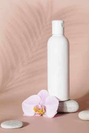 Mock up of white bottle lotion bottle with pink orchid flower, stone and tropical leaf shadow on beige background Natural organic cosmetics conceptの写真素材