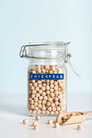 chickpeas in glass jar with wooden spoon on blue and white background. healthcare lifestyle and organic food concept.の写真素材