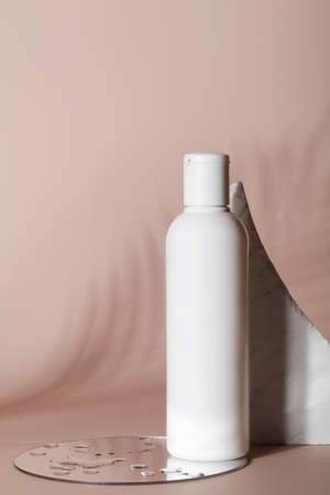 Mock up of white bottle lotion bottle with stone, mirror with water and tropical leaf shadow on beige background.Natural organic cosmetics concept.の写真素材