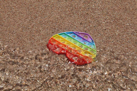 colorful antistress sensory pop up toy in form of heart on sand with water on beach. summer and relax concept. autism needs silicone stress relief toyの写真素材
