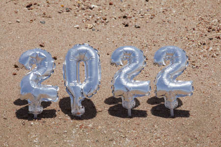 Christmas and happy new year concept. silver balloons in the form of numbers 2022 on the sand...