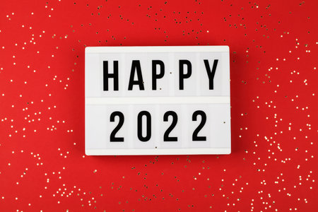 lightbox with words happy 2022 and holiday confetti on red background. top view new year...