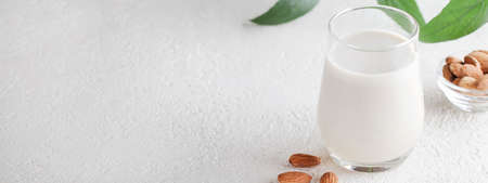 Vegan almond milk in glass with nuts and green plant on white background. Healthy vegetarian food. selective focus. Non dairy alternative milk. bannerの写真素材
