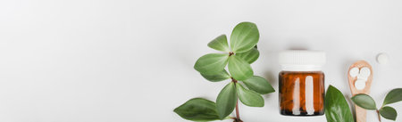 Herbal pills in glass bottle, wooden spoon and green plant leaves on white background. alternative medicine and healthy lifestyle. copyspace. bannerの写真素材