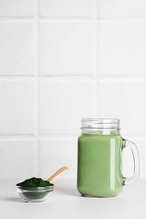 fresh green smoothie in glass bottle and spirulina powder with spoon on white background. useful habits, self care and healthy lifestyle. copy spaceの写真素材