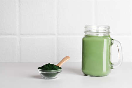 fresh green smoothie in glass bottle and spirulina powder with spoon on ceramic tile background. self care and healthy lifestyle. copy spaceの写真素材
