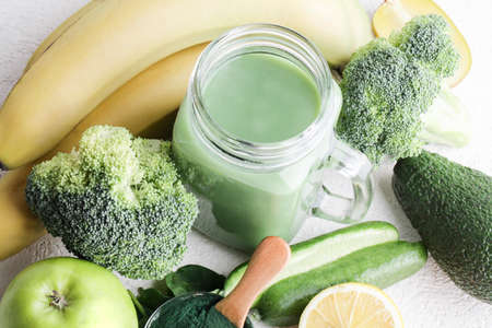 green smoothie in glass bottle, spirulina powder, vegetables and fruits on white ceramic tile background. healthy, raw, vegan diet concept. top viewの写真素材