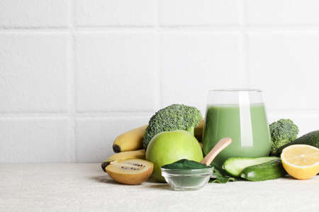green smoothie in glass, spirulina powder, vegetables and fruits on white ceramic tile background. healthy, raw, vegan diet concept. copy spaceの写真素材