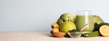 green smoothie in glass, spirulina powder, vegetables and fruits on blue background. healthy, raw, vegan diet concept. copy space bannerの写真素材