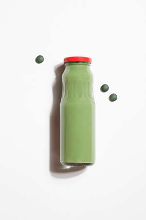 green smoothie in bottle and spirulina algae pills on white background. useful habits, self care and healthy lifestyle concept. healthy snack.の写真素材
