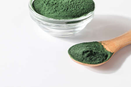 natural additives and superfood. green spirulina algae powder in glass with wood spoon on white background. healthy lifestyle concept. organic foodの写真素材