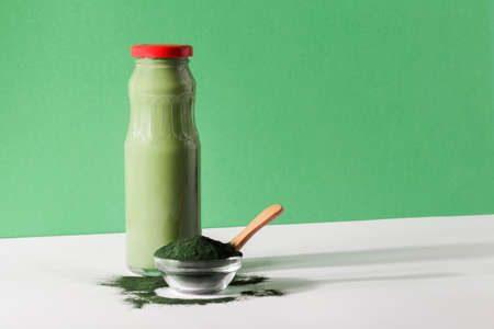 green smoothie in bottle and spirulina algae powder in glass bowl on green, white background.useful habits,self care and healthy lifestyle concept.の写真素材