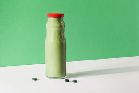 green smoothie in bottle and spirulina algae pills on green and white background. useful habits, self care and healthy lifestyle concept. quick snackの写真素材