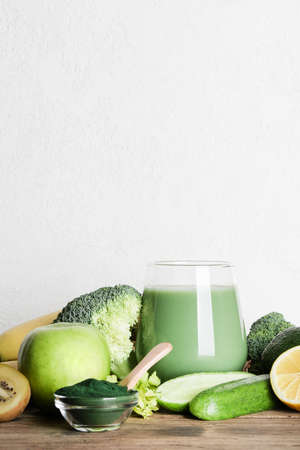 green smoothie in glass, spirulina powder, vegetables and fruits on wooden background. healthy, raw, vegan diet concept. copy spaceの写真素材