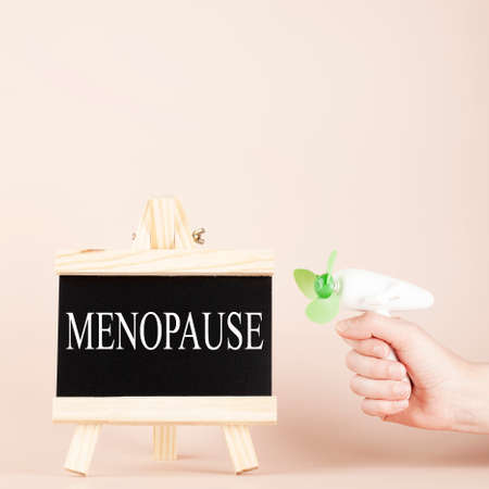 menopause word written on black board and hand holding fan on beige background. women health and middle age concept. squareの素材 [FY310187623548]