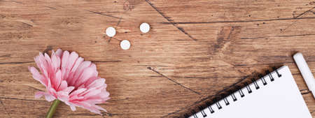 women health concept. medicine, health care style. copyspace. white pills, flower, notebook on brown wooden background. banner copy spaceの写真素材