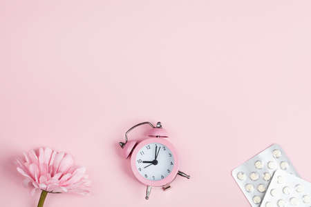 women health concept. copyspace. pills, flower and clock on pink background. wellness, medicine, personal and physical health.の写真素材
