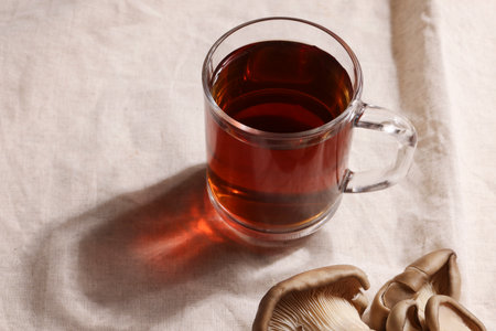 Natural medicine, reduce stress and improve immunity concept. Mushroom hot drink. Tea in glass mug with mushrooms on textile background. copyspace.の写真素材
