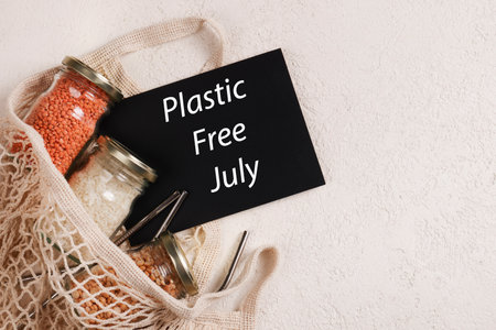 Zero waste lifestyle concept. Responsible consumption. Plastic free July written on black board with mesh , glass jar, reusable strawsの写真素材