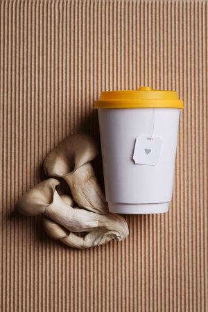 Natural medicine, reduce stress and improve immunity concept. Mushroom hot drink. Tea in takeaway cup with mushrooms on brown background.の写真素材