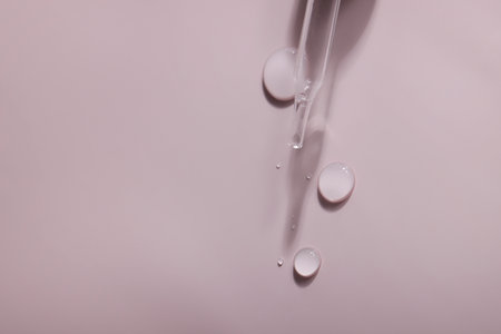 dense liquid, dripping, flowing, skincare concept. Cosmetic pipette with drops of serum, vitamin or oil on pink background. copy spaceの写真素材