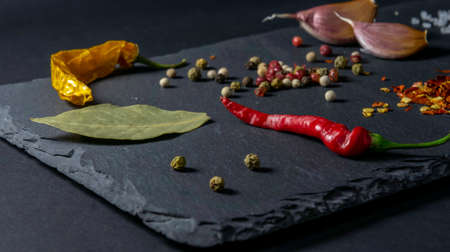 Spices on a stone plate. Black background. Black stone. Garlic, sea salt, pepper, chili, hot pepper, bay leafの写真素材