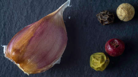 Garlic and pepper on a stone plate. Black background. Black stone. Close up. Macro