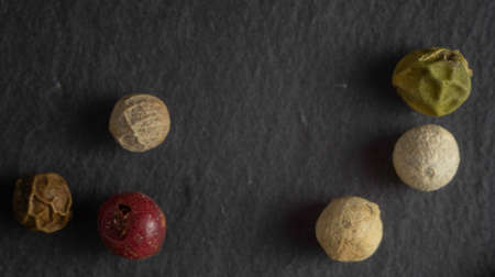 Pepper on a stone plate. Black background. Black stone. Close up. Macro