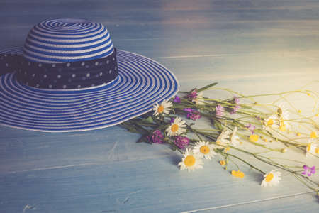 Female hat, striped, bouquet of wildflowers, top view. On a wooden background. Blue color. Conceptual imageの写真素材